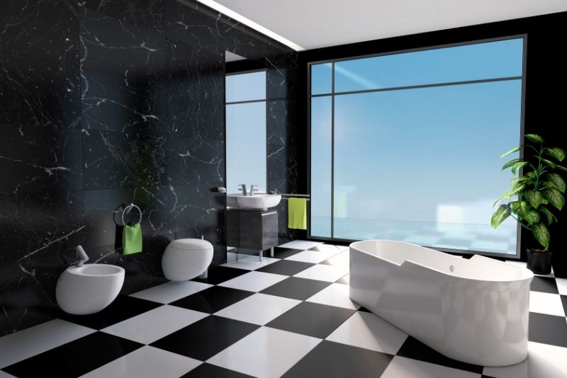 White freestanding bath, toilet and sink against a black wall with a large window